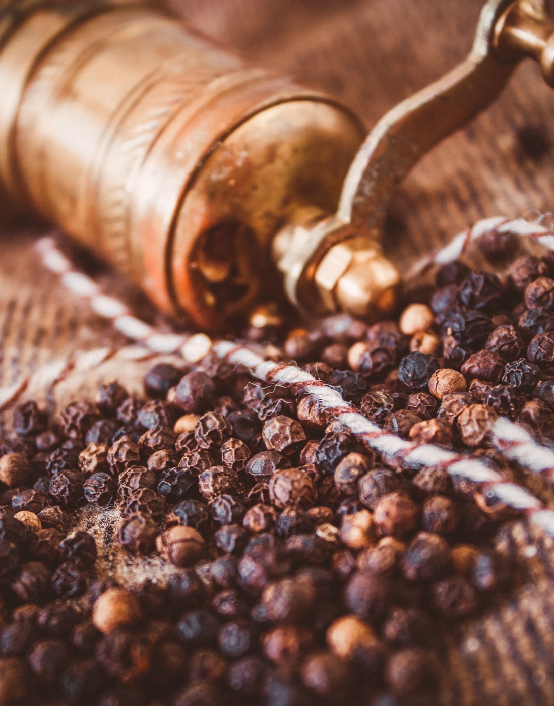 Black peppercorns beside a pepper grinder.
