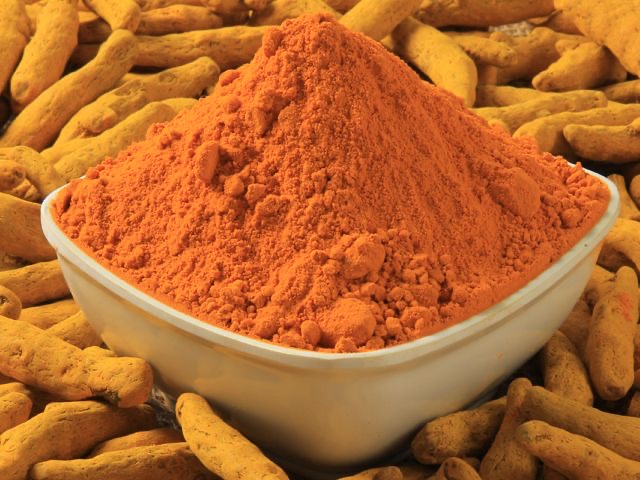 A bowl of ground turmeric surrounded by dried turmeric fingers.